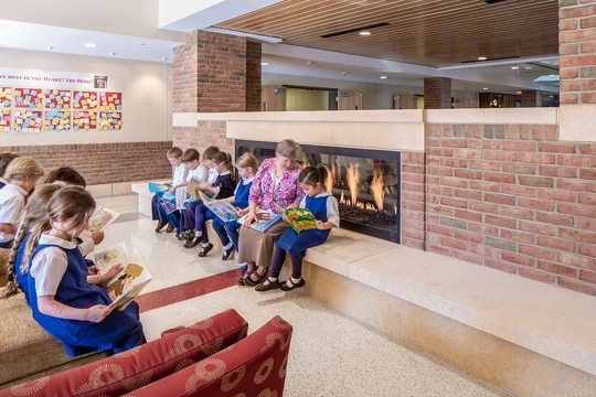 a teacher and young elementary students read in the Heart gathering area of Visitation School in Mendota Heights, Minnesota